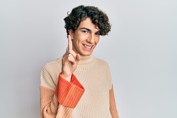 Hispanic young man wearing casual winter sweater showing and pointing up with finger number one while smiling confident and happy.