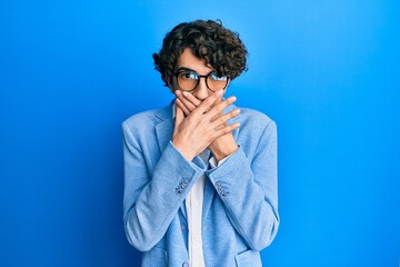 Fototapeta na wymiar Hispanic young man wearing business jacket and glasses shocked covering mouth with hands for mistake. secret concept.