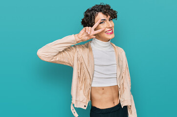 Handsome man wearing make up and woman clothes doing peace symbol with fingers over face, smiling cheerful showing victory