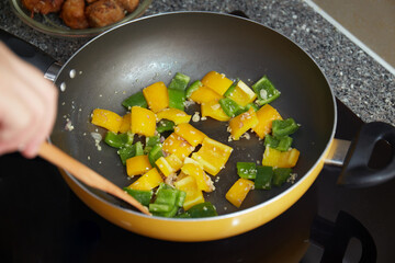 A closeup shot of yellow and green peppers being cooked in a frying pan
