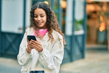 Beautiful hispanic girl smiling happy using smartphone and headphones at the city.