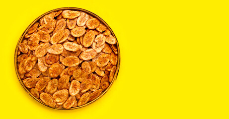 Banana chips in bamboo basket on yellow background.