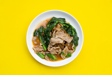 White plate of fried flat noodle with pork and kale in gravy sauce on yellow background.