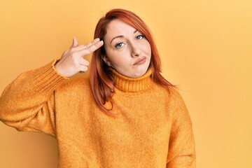 Beautiful redhead woman wearing casual winter sweater over yellow background shooting and killing...