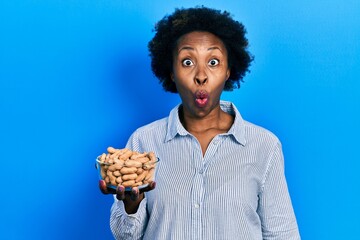 Young african american woman holding peanuts scared and amazed with open mouth for surprise, disbelief face