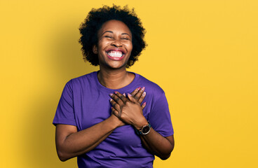 African american woman with afro hair wearing casual purple t shirt smiling with hands on chest...