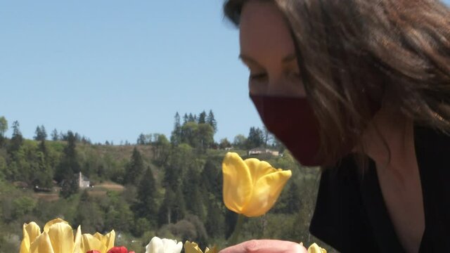 Woman wearing face mask walks through a field of tulips and trys to smell the flowers.