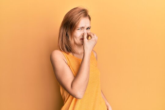 Young Caucasian Woman Wearing Casual Style With Sleeveless Shirt Smelling Something Stinky And Disgusting, Intolerable Smell, Holding Breath With Fingers On Nose. Bad Smell