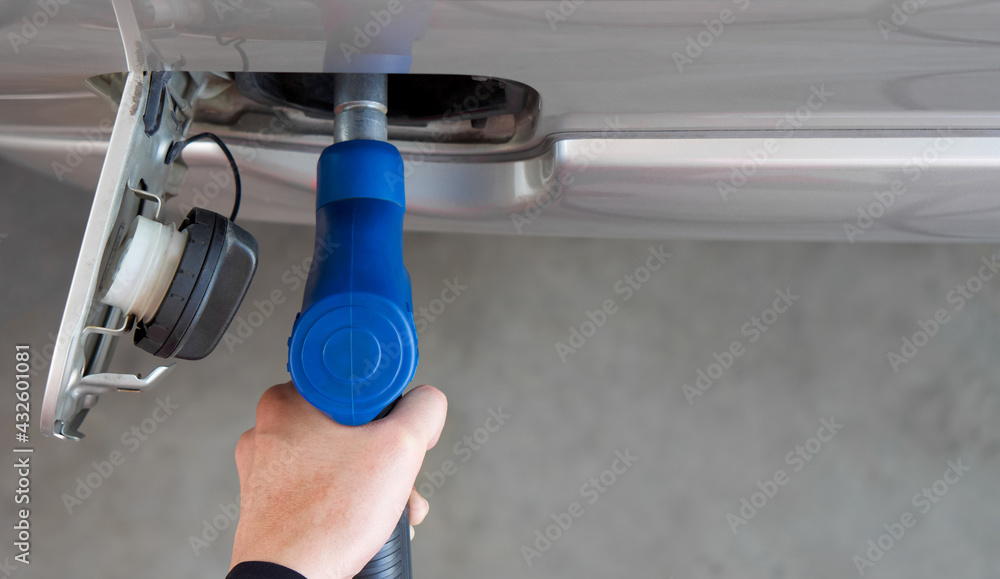 Wall mural closeup hand holding blue gas pump nozzle. gas station worker filling up bronze pickup truck tank (t