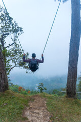 Vertical shot of a Hispanic man on a long swing with a view of the forest in Tekilatlakpan, Mexico