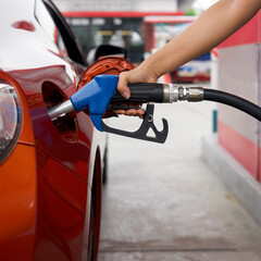 Gas station worker's hand holding blue benzene gas pump, filling up red sport car tank. Close up