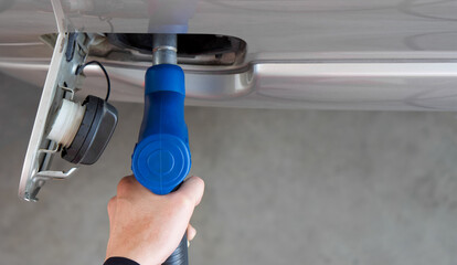 Closeup hand holding blue gas pump nozzle. Gas station worker filling up bronze pickup truck tank...