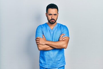 Handsome hispanic man with beard wearing blue male nurse uniform skeptic and nervous, disapproving expression on face with crossed arms. negative person.