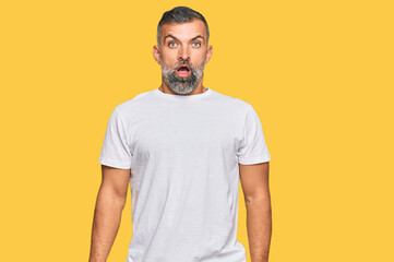 Middle age handsome man wearing casual white tshirt in shock face, looking skeptical and sarcastic, surprised with open mouth