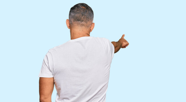 Middle age handsome man wearing casual white tshirt posing backwards pointing ahead with finger hand