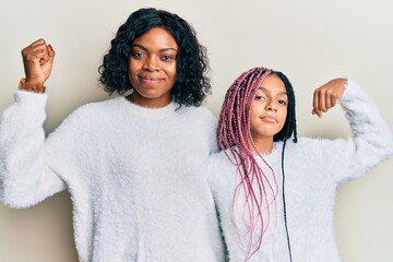 Beautiful african american mother and daughter wearing casual winter sweater strong person showing arm muscle, confident and proud of power - Powered by Adobe