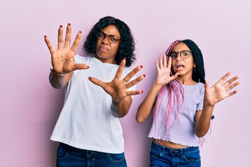 Beautiful african american mother and daughter wearing casual clothes and glasses afraid and terrified with fear expression stop gesture with hands, shouting in shock. panic concept.