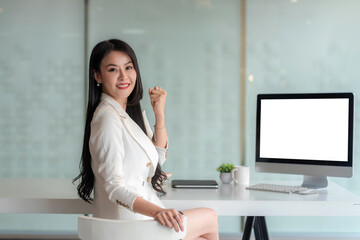 Young Asian businesswoman sitting in facing looking at camera with  computer blank white screen placed at an office table.