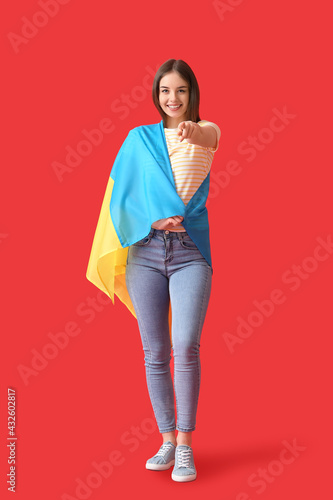 Beautiful young woman with Ukrainian flag on color background