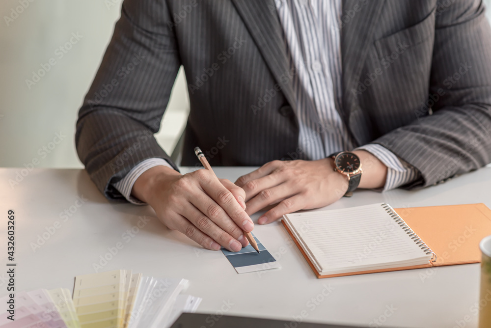 Poster close-up man designer holding a pencil pointing at a color sample of the notebook placed at the offi