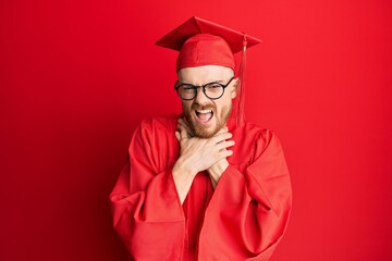 Young redhead man wearing red graduation cap and ceremony robe shouting and suffocate because painful strangle. health problem. asphyxiate and suicide concept.