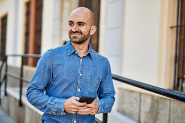 Young hispanic man smiling happy using smartphone at the city.