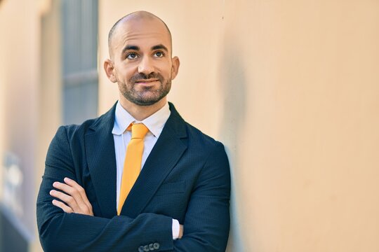Young hispanic bald businessman with arms crossed smiling happy at the city.