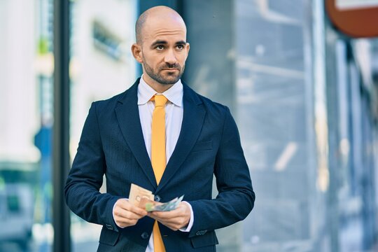 Young hispanic bald businessman with serious expression counting canadian dollars banknotes at the city.