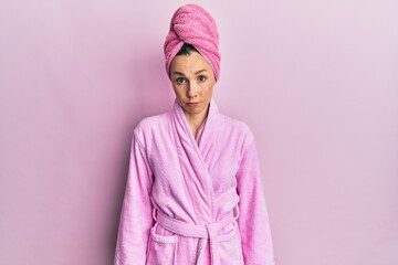 Young blonde woman wearing shower towel cap and bathrobe skeptic and nervous, frowning upset because of problem. negative person.