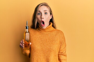 Young blonde woman holding olive oil can scared and amazed with open mouth for surprise, disbelief...