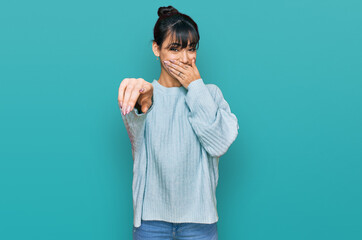 Young hispanic woman wearing casual clothes laughing at you, pointing finger to the camera with hand over mouth, shame expression