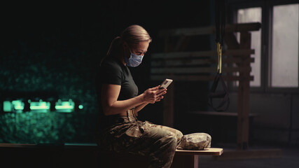 Military woman in mask using smartphone