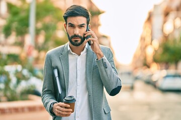 Young hispanic businessman with serious expression talking on the smartphone and drinking coffee at the city.