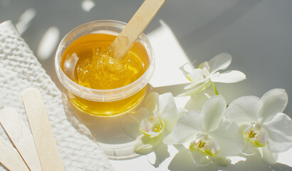 Sugar paste or wax honey in a transparent jar on a white background. Sugaring. Depilation and beauty concept. Waxing. - obrazy, fototapety, plakaty