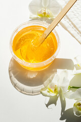 Sugar paste or wax honey in a transparent jar and white orchid on a white background. Sugaring. Depilation and beauty concept. Waxing.