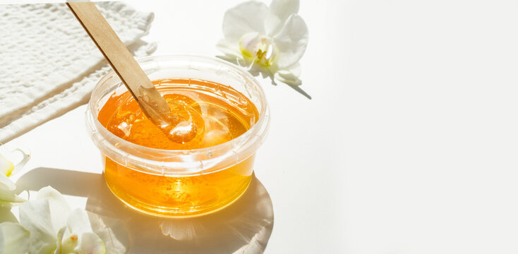 Sugar paste or wax honey in a transparent jar and white orchid on a white background. Sugaring. Depilation and beauty concept. Waxing.