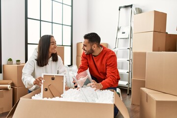 Young latin couple smiling happy unboxing cardboard box at new home.
