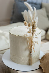 Amazing minimalistic cake cream beige decorated by dry ear of wheat cotton in boho scandi style