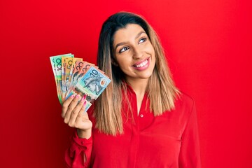 Beautiful brunette woman holding australian dollars smiling looking to the side and staring away thinking.