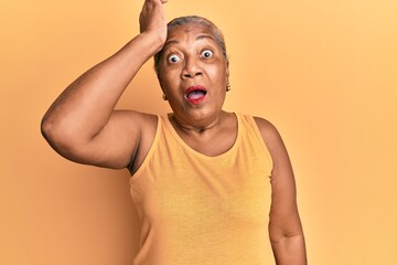 Senior african american woman wearing casual style with sleeveless shirt surprised with hand on...