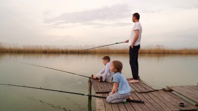 Dad and son and daughter on a wooden bridge catch fish from the river. 