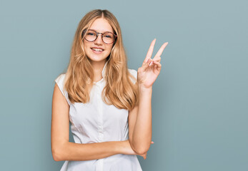 Beautiful young caucasian girl wearing casual clothes and glasses smiling with happy face winking at the camera doing victory sign. number two.