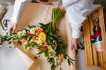 a female florist in a white shirt wraps a bouquet of fresh flowers in paper. Top view