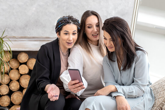 Group happy female friends chatting surfing internet use smartphone smiling having positive emotion
