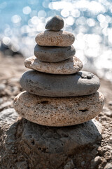 Fototapeta na wymiar A tower of stones. Balanced pyramid of pebbles on the beach on a sunny day. Blue sea in the background. Selective focus, bokeh. Zen stones on the sea beach, meditation, spa, harmony, tranquility