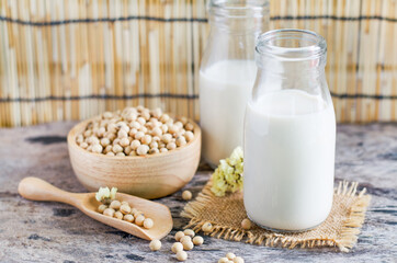 Closed up delicious homemade soybean milk in glass bottle over blur seeds in wooden bowl and spoon, for clean food homemade product or agricultural goods concept