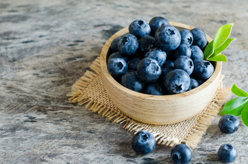 Closed up fresh blueberry fruit with green leaf in wooden bowl