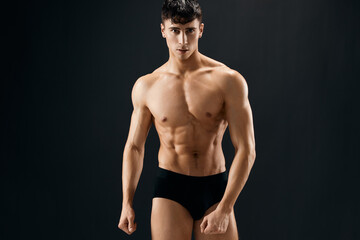 man in black shorts with a pumped-up body bodybuilder dark background