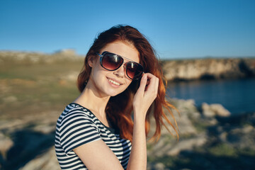 beautiful red-haired woman in a t-shirt and sunglasses on nature in the mountains near the river