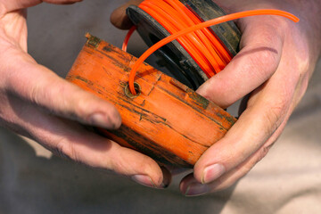 a man collects a grass trimmer reel after replacing the fishing line in it